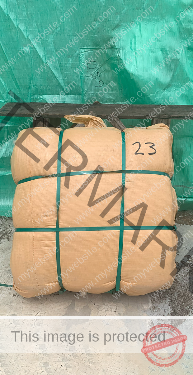 Small 25 kg sack wrapped in green plastic straps, placed on a cracked concrete floor, with a green tarp in the background.